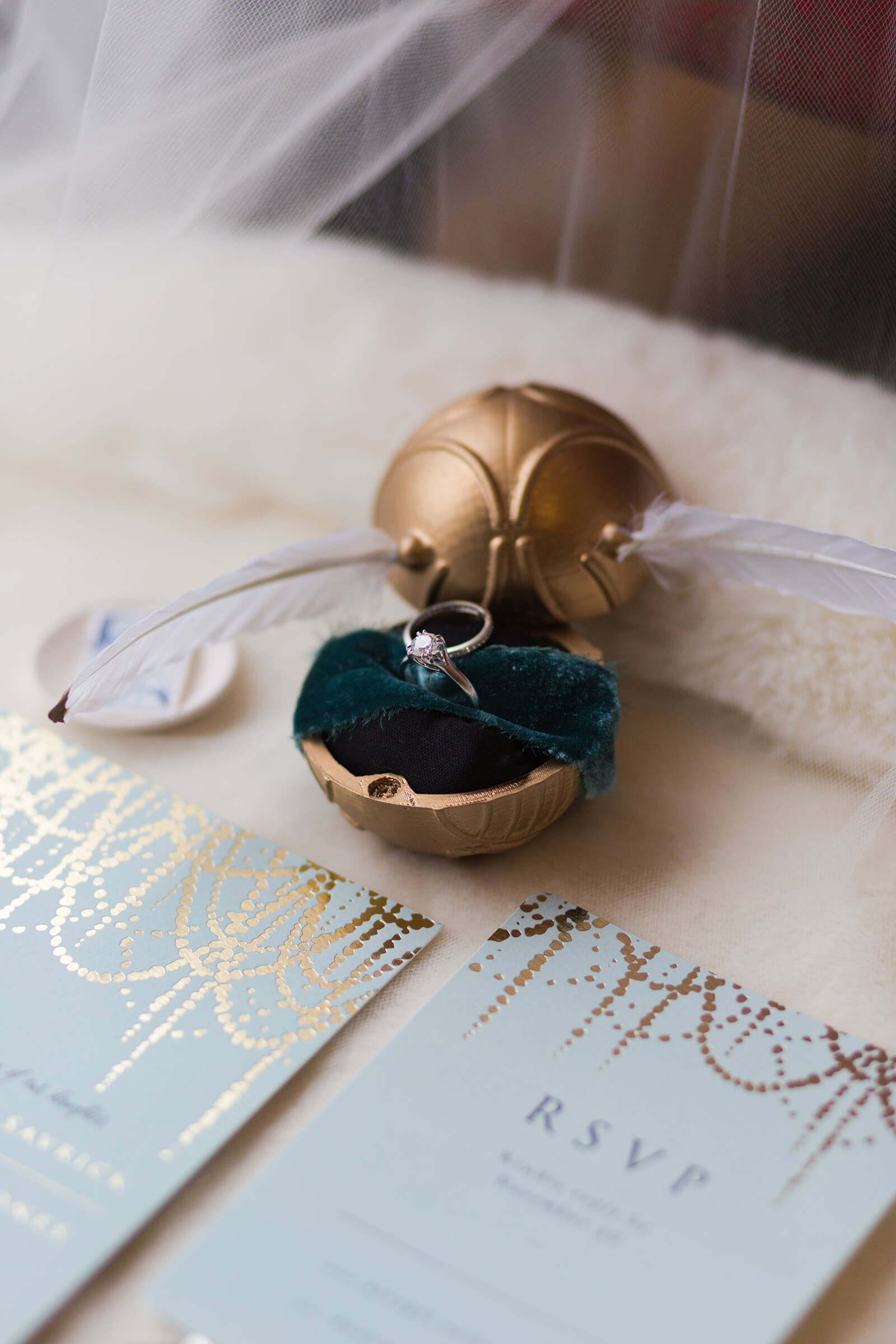 golden snitch from Harry Potter holds wedding ring on invitation suite at Hotel Zaza captured by Swish and Click Photography