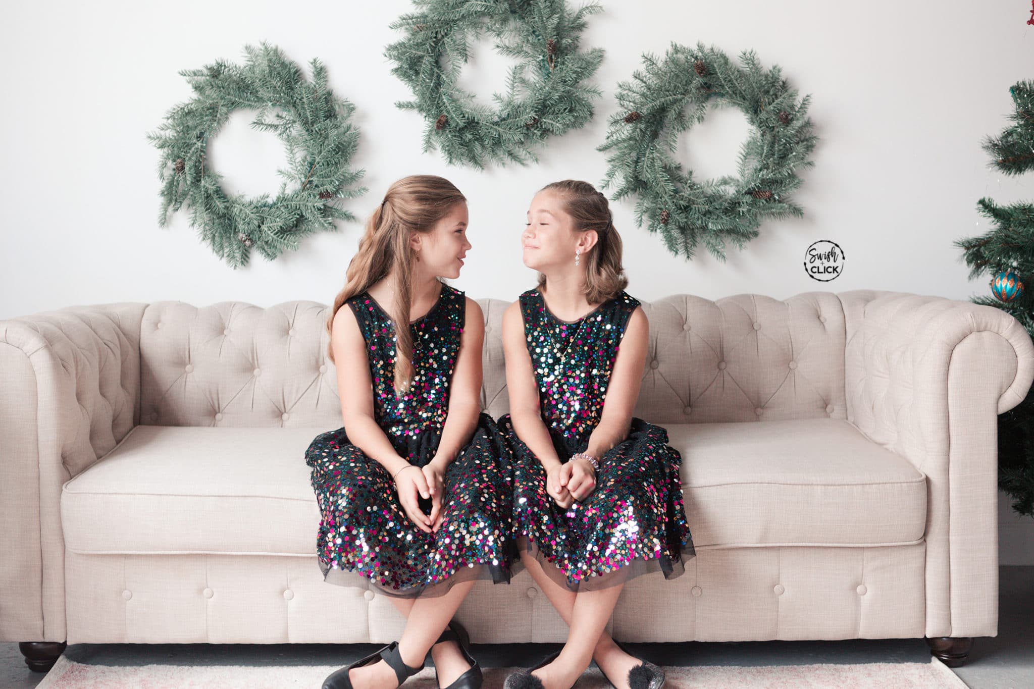 sisters smile at each other during their Christmas portraits in Houston Texas by Swish and Click Photography