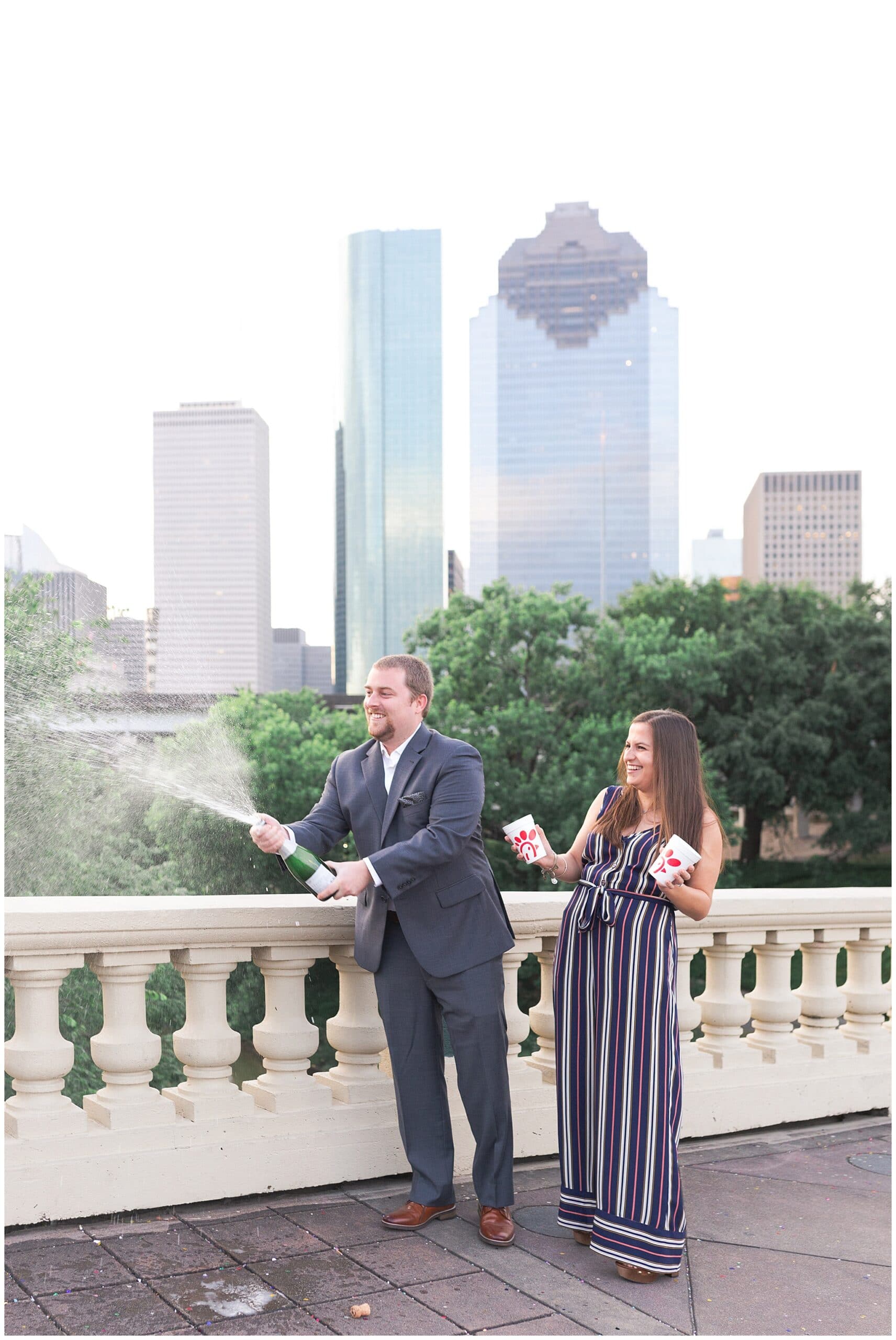 couple popping champagne on Sabine St bridge during engagement session by Swish and Click Photography