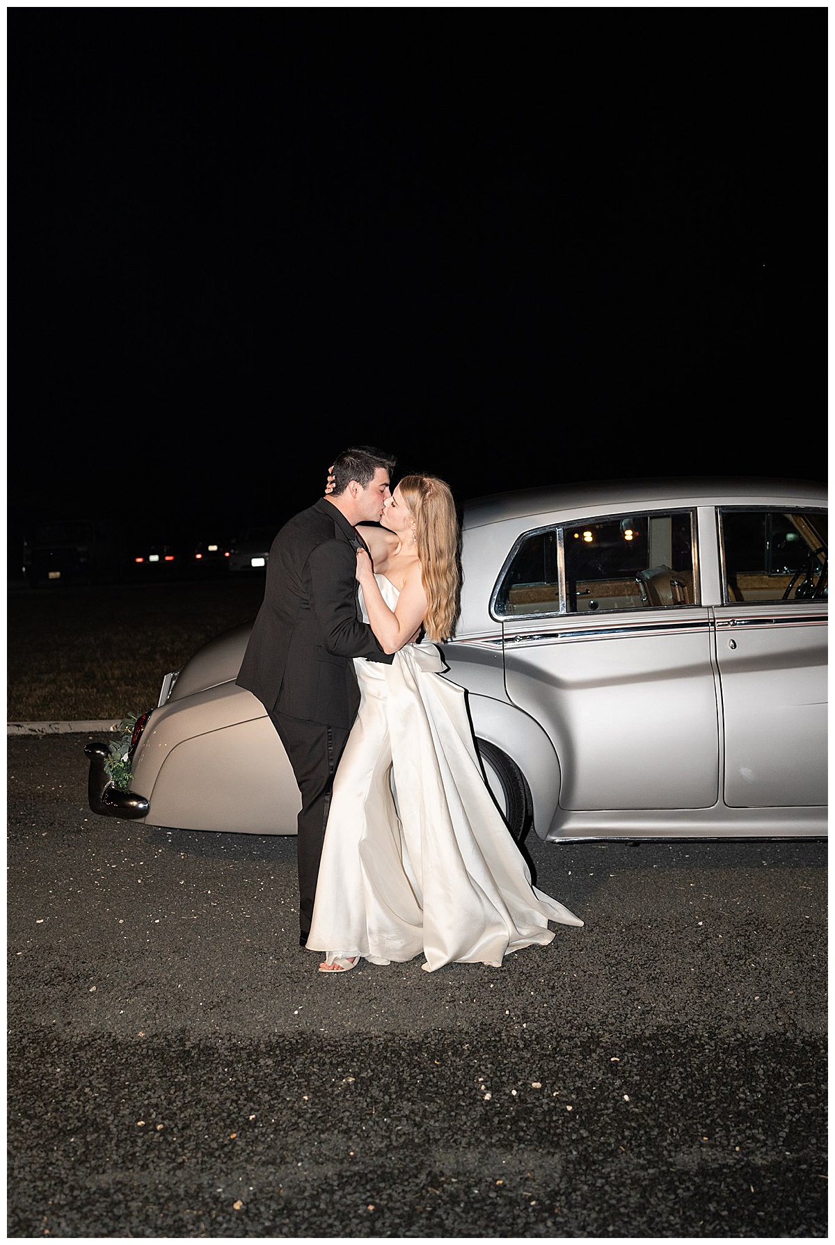 Bride and groom share a kiss in front of old classic car at The Homestead