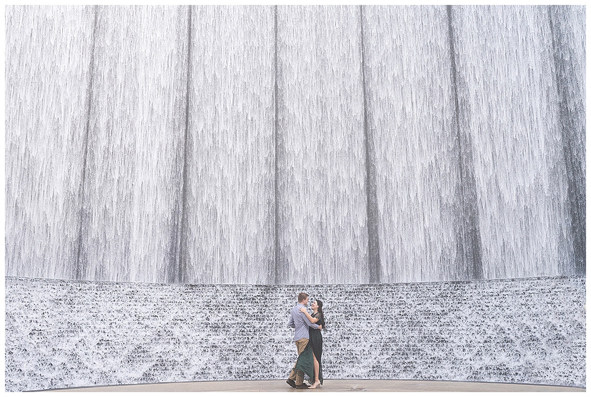 Adult stand close together in front of waterfall for Arboretum Engagement session