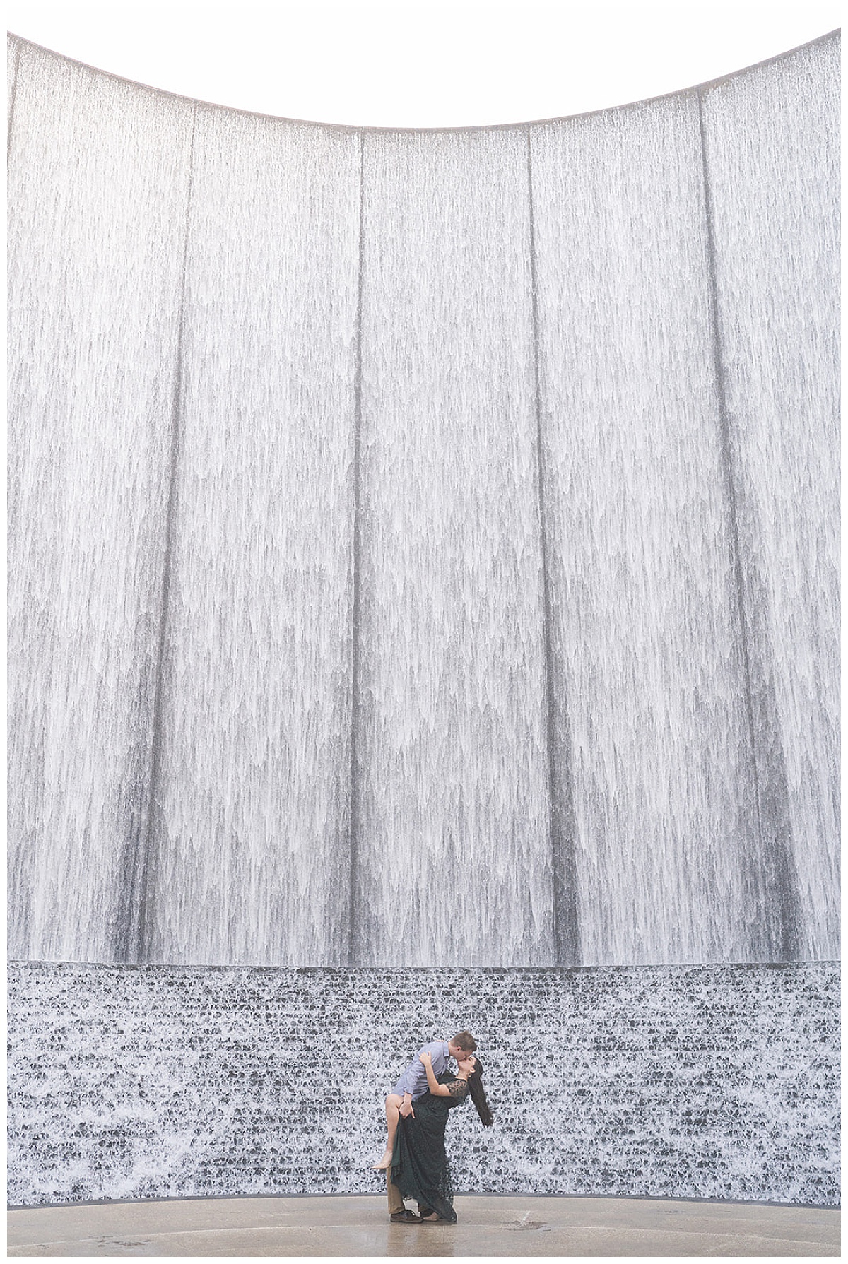 Couple holds one another close in front of waterwall during Arboretum Engagement Session