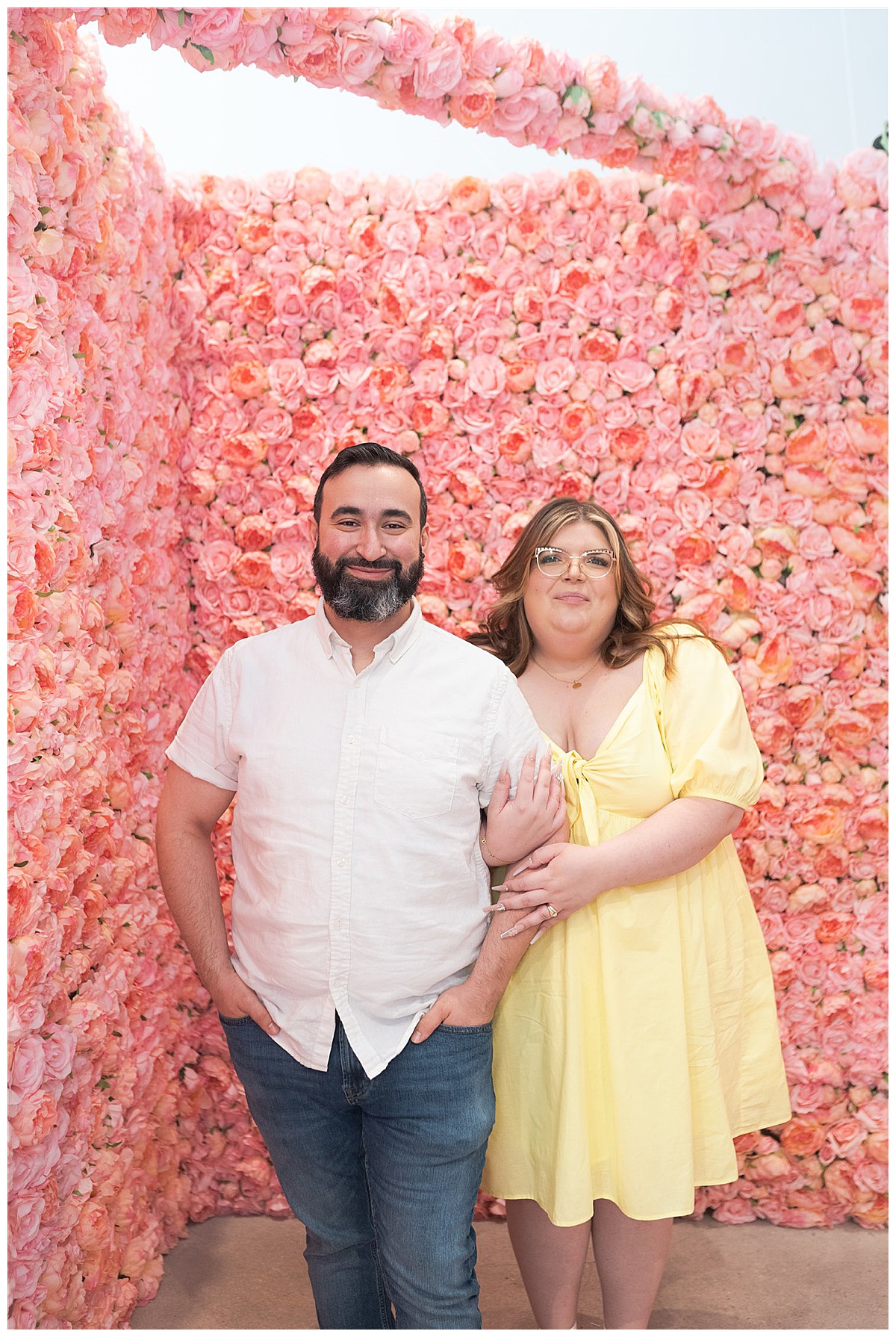 Two people stand in front of flower wall at Flower Vault Engagement