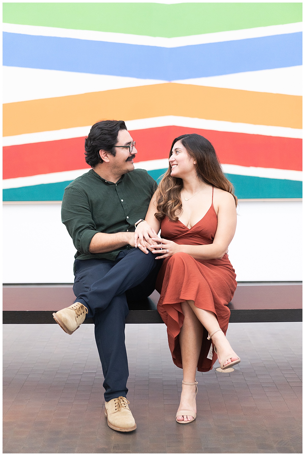 Engaged couple sit together in front of art for Houston’s Best Wedding Photographers