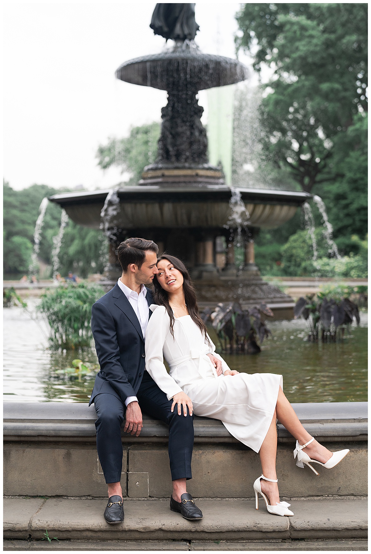 Man and woman cuddle in close together near a fountain during their Destination Engagement Session