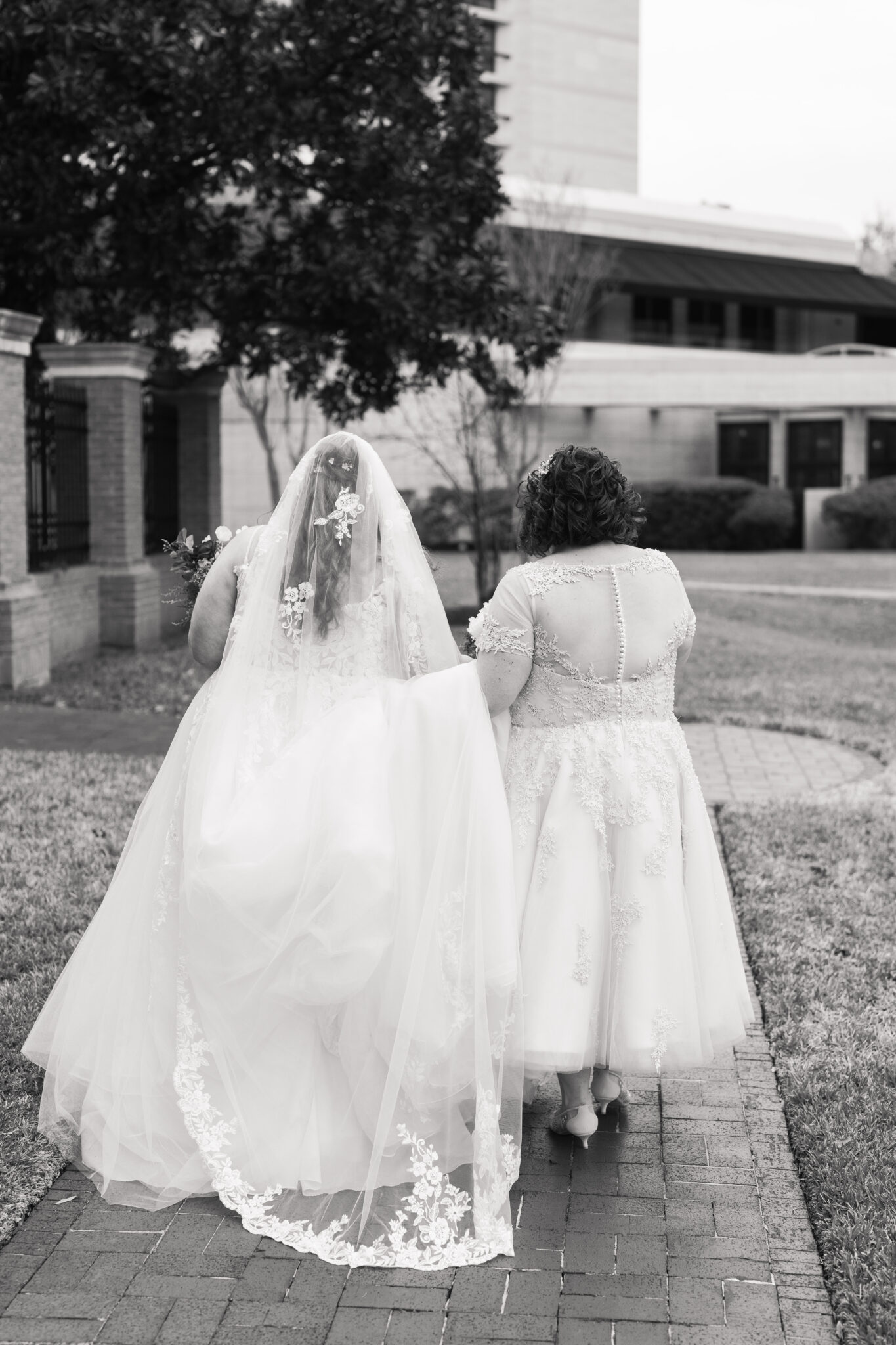 Two curvy brides walking hand in hand through a garden.