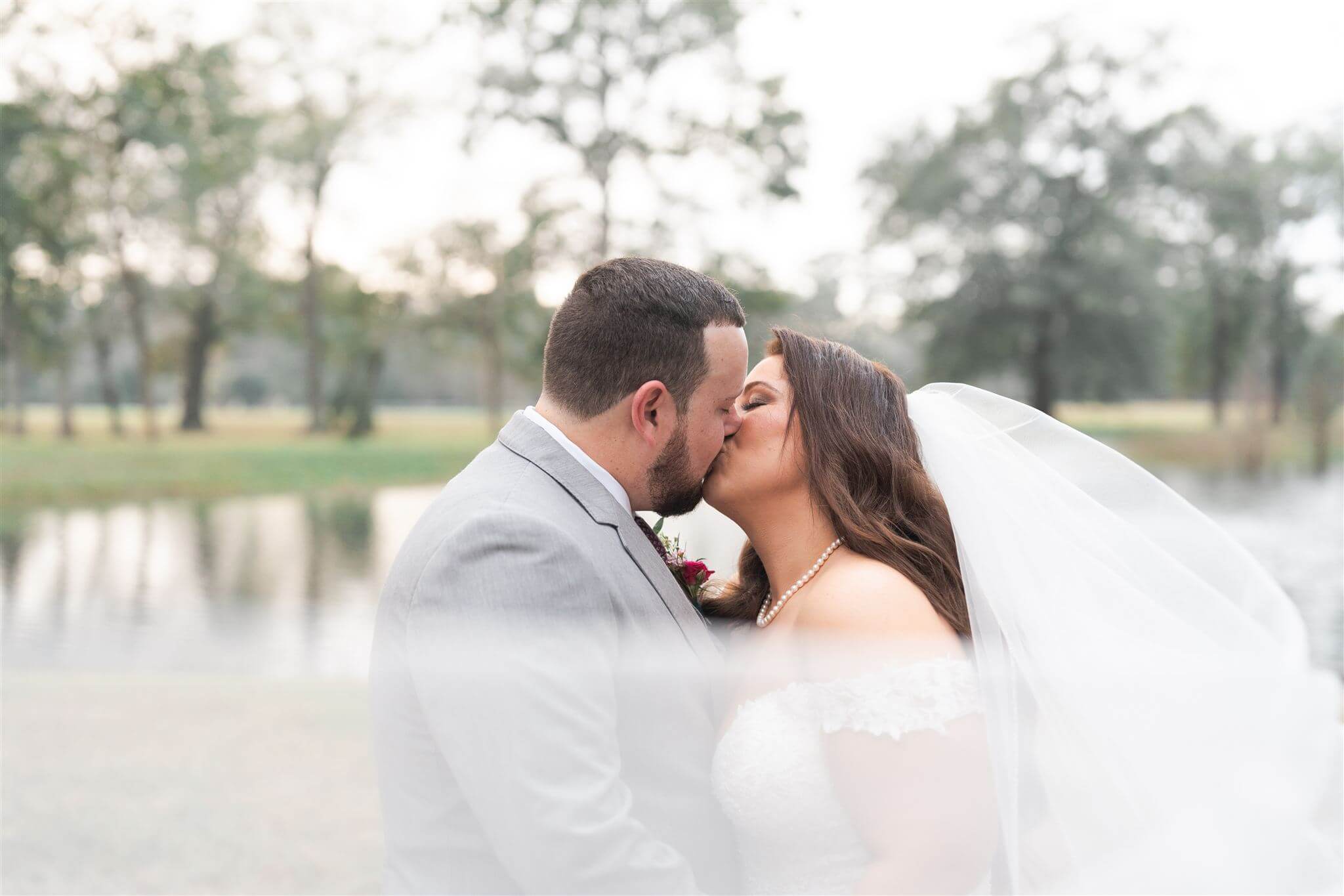 A veil creating a dramatic moment as it swoops around a groom and curvy bride as they kiss.