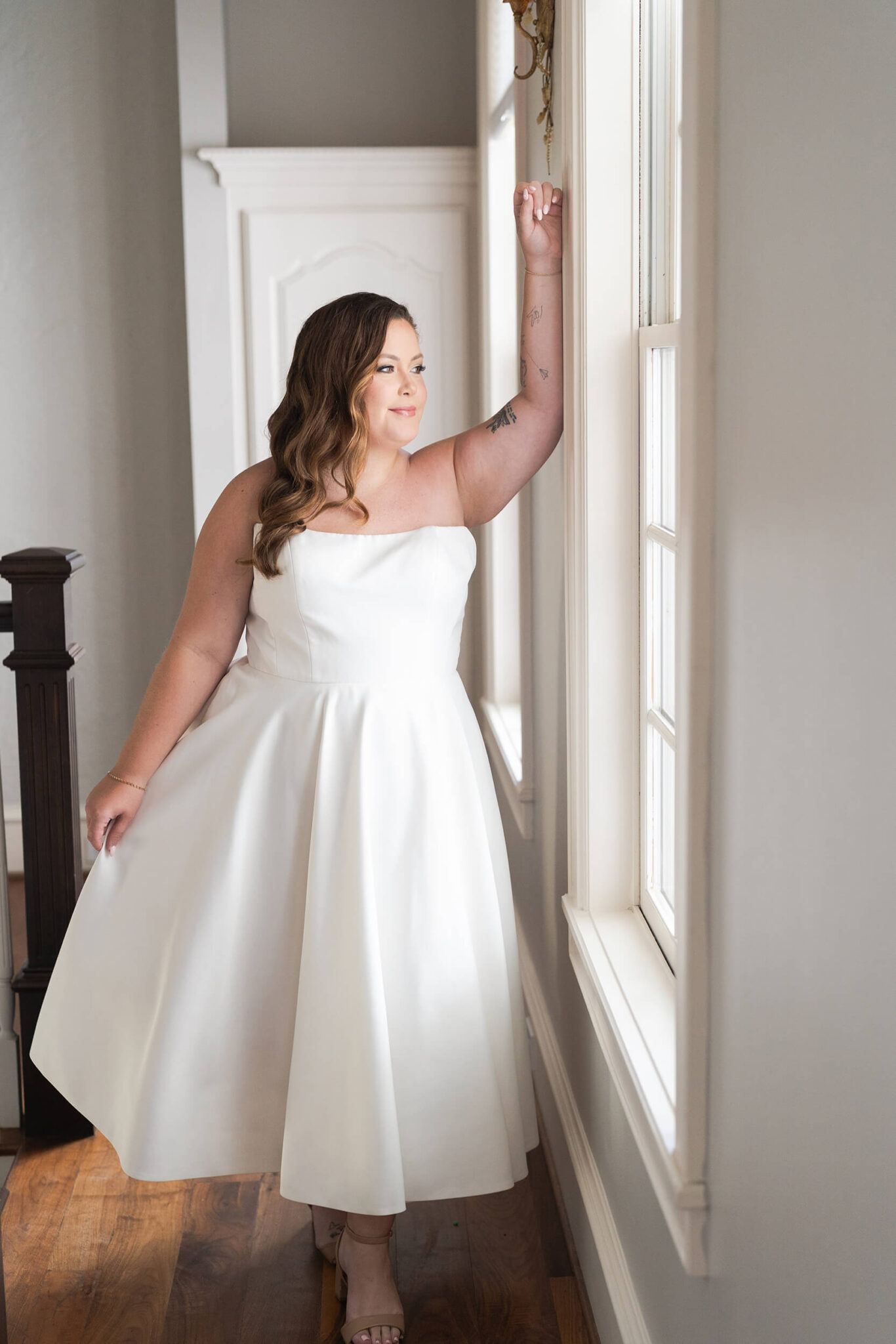 Facing straight on and looking out the window, a curvy bride smiles at Sandlewood Manor in Houston Texas